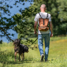 Load image into Gallery viewer, A man walking outdoors on a grassy path with a dog on a leash, wearing a brown leather backpack. The man is seen from behind, wearing a white t-shirt and blue jeans, with green trees and blue sky in the background.