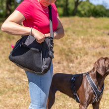 Load image into Gallery viewer, Person holding a black bag with a dog wearing a harness in an outdoor setting