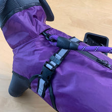 Load image into Gallery viewer, A close-up of a purple waterproof dog coat with black mesh and rubber details, a black zipper, and a purple-and-black rope leash attachment, shown on a light wood floor.
