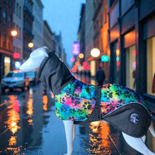 Load image into Gallery viewer, Colorful dog coat with paw pattern on a wet city street at night.
