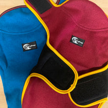 Load image into Gallery viewer, Two dog vests, one blue and one maroon, with visible brand logos on a wooden surface.
