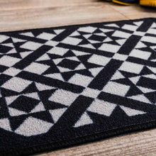 Load image into Gallery viewer, Geometric patterned rug with black and white design on a wooden floor
