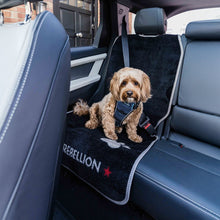 Load image into Gallery viewer, Dog sitting on a black car seat cover with 'Rebellion' branding in a vehicle.
